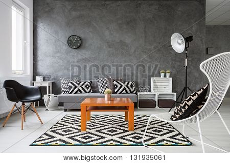 Living room with grey walls and white wooden parquet. Black and white decorations with orange coffee table in the middle of the room