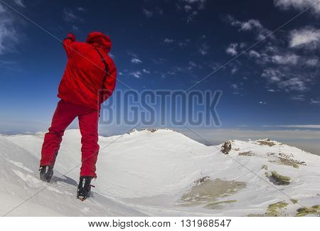 man standing on a cliff in mountains with snowy picks and blue sky with clouds on background