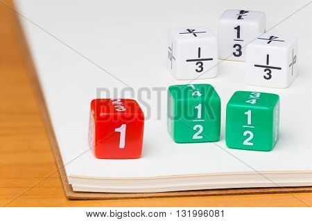 Colored fraction dices on blank white paper notebook on wooden desk selective focus on dices