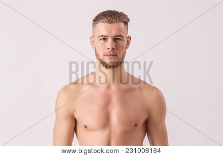 Studio shot of handsome naked man looking to camera while standing isolated on white background. Young bearded hipster standing against white background. Concept of men's masculinity and confidence