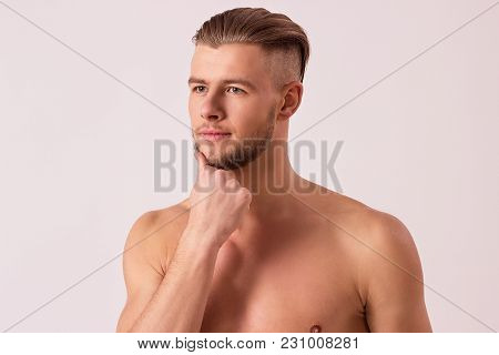 Portrait of attractive bearded man touching chin with hand and looking away while isolated on white background. Young thoughtful hipster standing against white background. Masculine and confident man