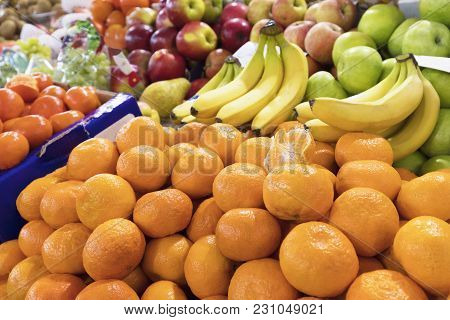Bright Background Of Fresh Fruits. Mandarins, Bananas, Apples Lie In The Trays In The Market And Att