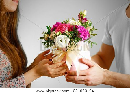 The Guy Gives A Bouquet Of Flowers To A Girl. Composition Of Flowers In A Pink Hatbox. Tied With Wid
