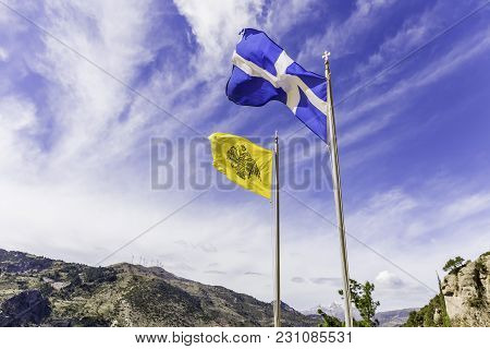 Greek And Byzantine Flags Waving On The Air Against Cloudy Sky