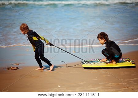 Brother And Sister Playing With Their Bodyboards On The Beach And In The Shore Break During A Summer