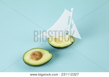 Avocado Half With White Sail On A Turquoise Background. Minimal And Quirky Color Still Life Photogra