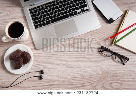 Top View Of Laptop And Notepad With Glasses And Headphones On Rustic Wood Desktop And Cup Of Coffee.