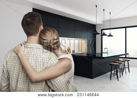 Back View Of Young European Couple Cudding In Creative Kitchen Interior With Panoramic City View. Dr
