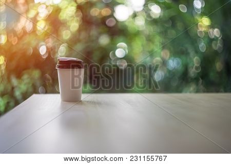 Blurred Disposable Coffee Cup On Wooden Table Over Garden Landscape With Sunlight. Beauty Nature Bac