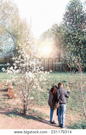 Happy Young Girl And Boy Teenagers Group Embraced Look At Spring Bloomy Trees And Dream At Garden Pa