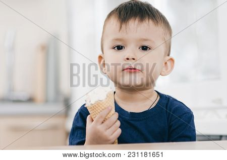 A Child In A Dark-blue T-shirt In The Bright Kitchen Eating A Waffle Ice Cream Cone In The Summer Ho
