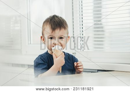 A Child In A Dark-blue T-shirt In The Bright Kitchen Eating A Waffle Ice Cream Cone In The Summer Ho