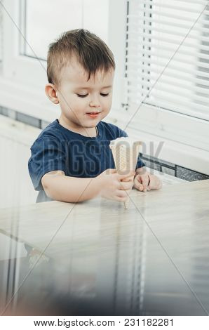 A Child In A Dark-blue T-shirt In The Bright Kitchen Eating A Waffle Ice Cream Cone In The Summer Ho