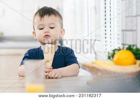 A Child In A Dark-blue T-shirt In The Bright Kitchen Eating A Waffle Ice Cream Cone In The Summer Ho
