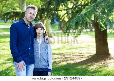 Handsome middle-aged man in park with his son. Attractive mid adult male model posing outddor with teen boy.