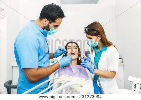 Smiling Beautiful Patient Sitting In Chair With Dental Purple Bib, Male Dentist, In Blue Uniform And