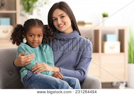 Young woman with little African-American girl indoors. Child adoption