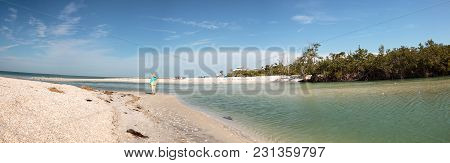 Older Woman Stands On The White Sand Beach In Front Of Aqua Blue Water Of Clam Pass