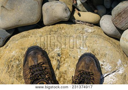 Hiking Boots, Boulders And Colorful Pebbles On The Beach On A Warm Summer Day