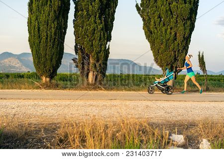 Running Mother With Child In Baby Stroller Enjoying Sunset And Mountains Landscape. Jogging Or Power