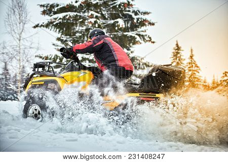 A Man Is Riding An Atv In Winter On The Snow In His Helmet.
