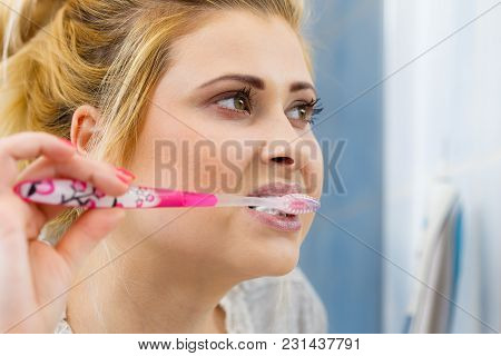 Woman Brushing Cleaning Teeth Closeup. Blonde Girl With Toothbrush In Bathroom, Looking At Mirror. O
