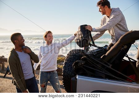 Three young adult male friends unloading backpacks from jeep