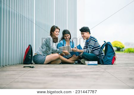 Smling College Student Showing Something Interesting On Tablet Computer To Her Friends