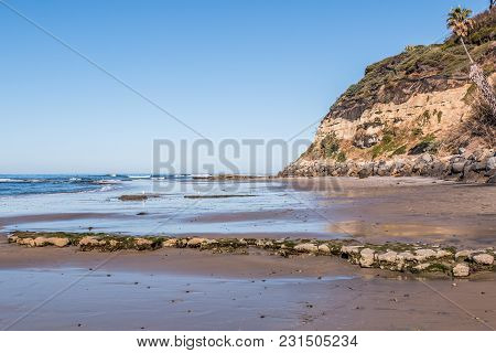 An Empty Swami Beach At Low Tide, With View Of Cliff And Rocky Reef Covered In Algae.