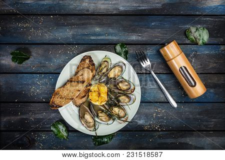 Mussels And Bread Toasts On On A White Plate. Served With Half Grilled Lemon, Fork And Leaves Of Kaf