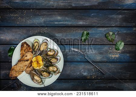 Mussels And Bread Toasts On On A White Plate. Served With Half Grilled Lemon, Fork And Leaves Of Kaf