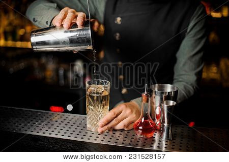 Barman Puring A Sweer Alcoholic Drink From Shaker Into A Cocktail Glass On The Bar Counter Against D