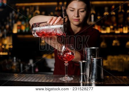 Beautiful Female Barman Pouring Sweet Red Alcoholic Drink Into A Cocktail Glass With Ice Cube