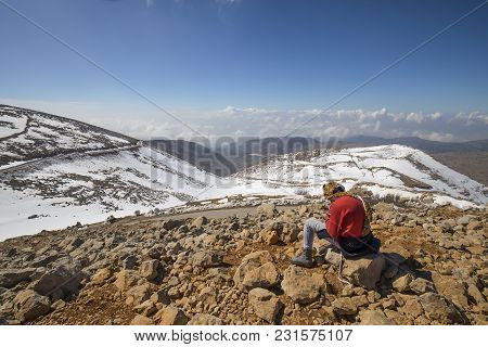 A Young Man Sitting On A Hill Overlooking Snowy Mountains