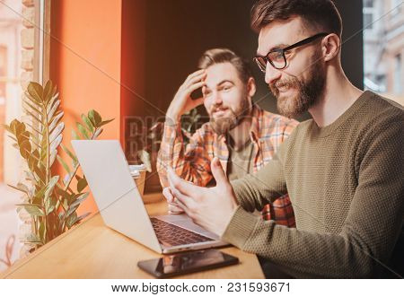 Close Up Of Two Friends Sitting At The Table And Looking To The Laptop's Screen. One Of Them Emotion