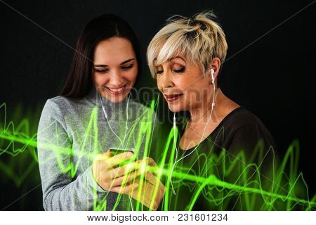 An Elderly Woman And A Young Girl Listen To Music Together. Communication Between People Of Differen