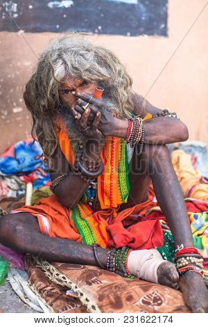 VARANASI, INDIA - MAR 16, 2018: Hindu sadhu smoking ganja, marihuana with chillum  on the ghats of the Ganges river. According to legends, the city was founded by God Shiva about 5000 years ago.