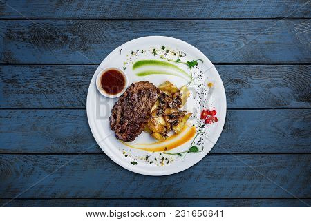 Horsemeat Steak With Potatoes And Mushrooms, Served On The White Plate With Wooden Background. Top V