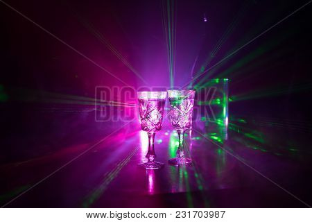 Two Glasses Of Vodka With Bottle On Dark Foggy Club Style Background With Glowing Lights (laser, Sto