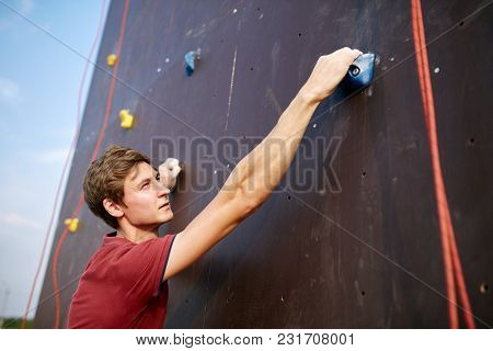 Back View Close-up Of Climber Hands On A Rock Hook Of The Artificial Climbing Wall Outdoors. Young H