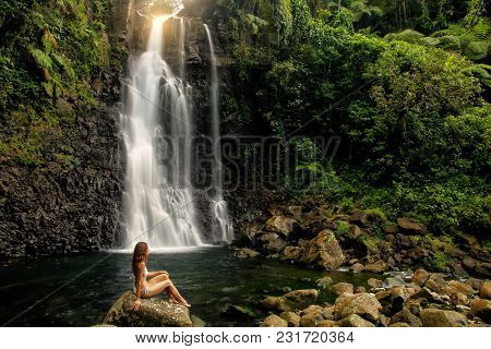 Young Woman In Bikini Sitting By Middle Tavoro Waterfalls In Bouma National Heritage Park On Taveuni