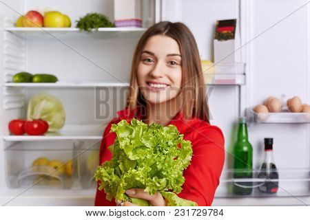 Cheerful Beautiful Female Holds Salad Lettuce In Hands, Supports Healthy Nutrition, Stands Near Frid