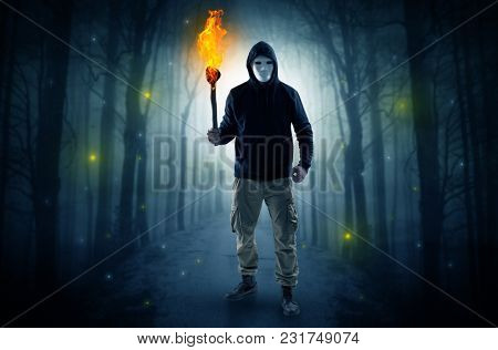 Mysterious man coming from a path in the forest with burning flambeau concept