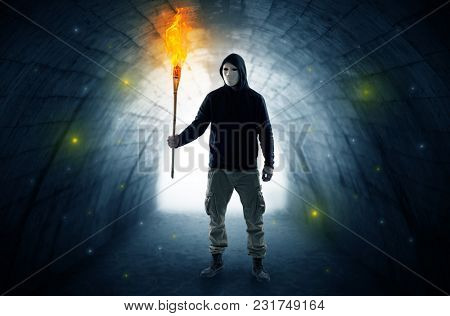 Ugly man with burning flambeau walking in a dark tunnel
