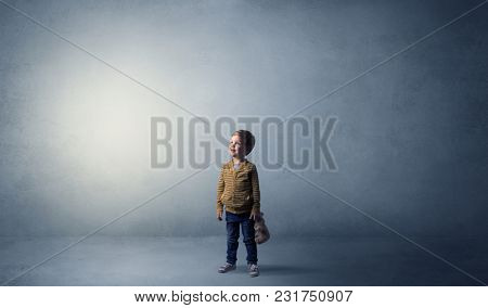 Little waggish kid staying alone in a big empty room with his plush