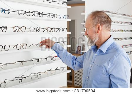 Elderly Man Choosing Corrective Glasses In Optics Store