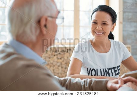 Welfare Volunteering. Cheerful Jovial Volunteer Smiling While Speaking To Senior Man And Looking At 