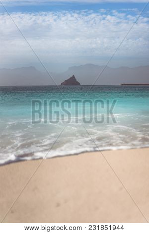 Black Rock On Ocean Horizon. Defocused Ocean Wave Rolling To Sandy Beach With Clear Transparent Azur