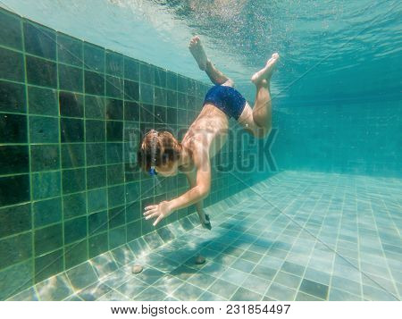 A Child Boy Is Swimming Underwater In A Pool, Smiling And Holding Breath, With Swimming Glasses.