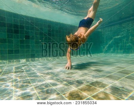 A Child Boy Is Swimming Underwater In A Pool, Smiling And Holding Breath, With Swimming Glasses.